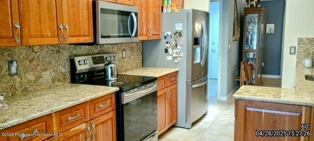 kitchen featuring light tile patterned floors, backsplash, appliances with stainless steel finishes, and brown cabinetry