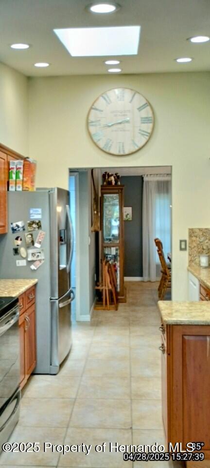kitchen featuring appliances with stainless steel finishes, light tile patterned flooring, a high ceiling, and a skylight