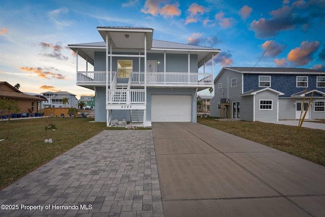 beach home featuring a garage, a balcony, covered porch, and a lawn