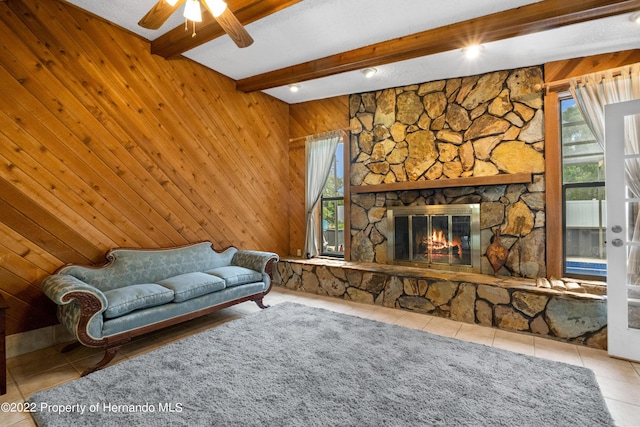 living room with a stone fireplace, tile patterned flooring, beam ceiling, and wood walls