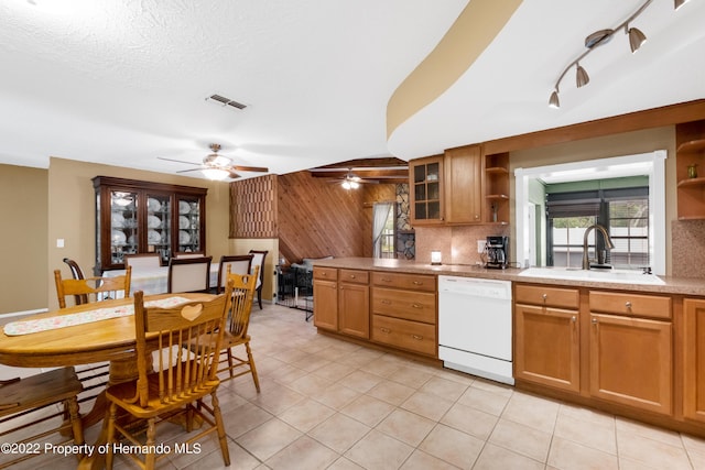 kitchen featuring sink, light tile patterned floors, dishwasher, tasteful backsplash, and wood walls