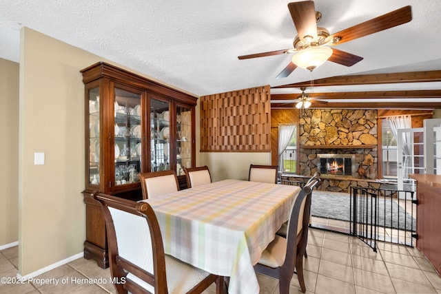 tiled dining room with beamed ceiling, ceiling fan, a fireplace, and a textured ceiling