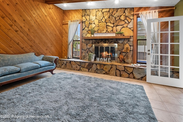 living room featuring tile patterned flooring, wooden walls, a stone fireplace, french doors, and beamed ceiling