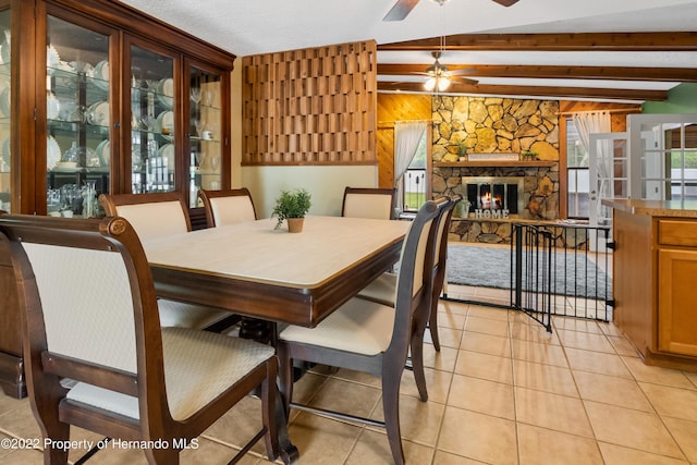 tiled dining area featuring a stone fireplace, vaulted ceiling with beams, and ceiling fan