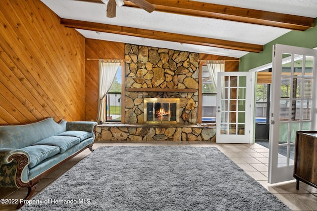 living room with vaulted ceiling with beams, a textured ceiling, light tile patterned floors, wooden walls, and a fireplace