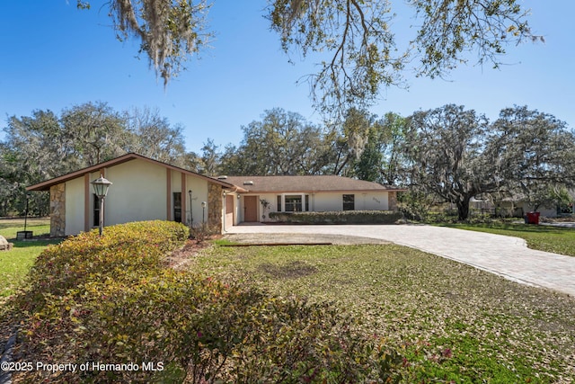 ranch-style house featuring stucco siding, decorative driveway, and a front yard