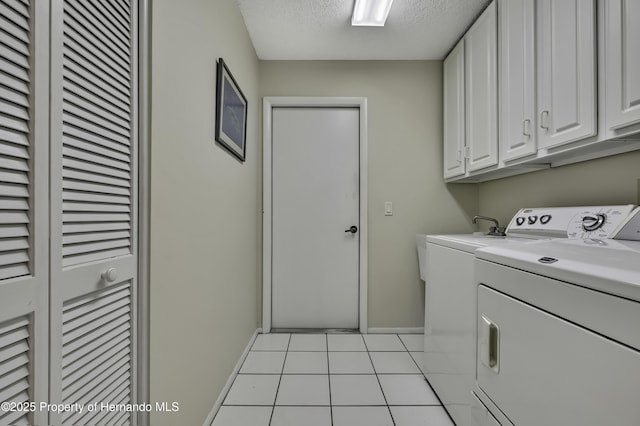 clothes washing area with cabinets, washer and dryer, light tile patterned floors, and a textured ceiling