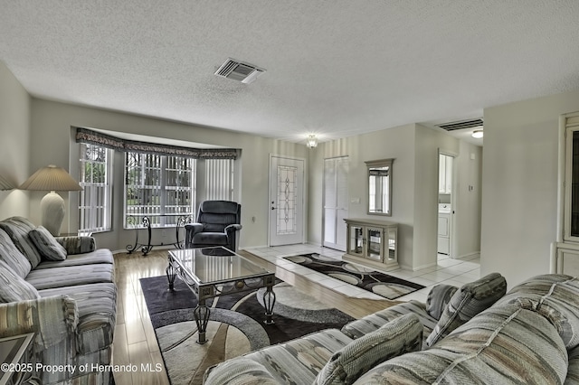 living room featuring washer / dryer, a textured ceiling, and light wood-type flooring