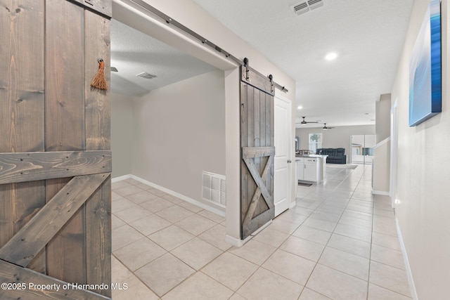 hallway with light tile patterned flooring, a barn door, and a textured ceiling