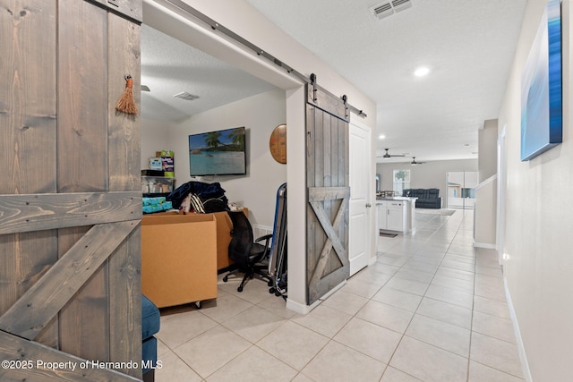 corridor featuring light tile patterned floors, a barn door, and a textured ceiling