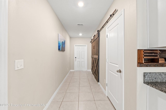 hallway with light tile patterned flooring, a barn door, and a textured ceiling