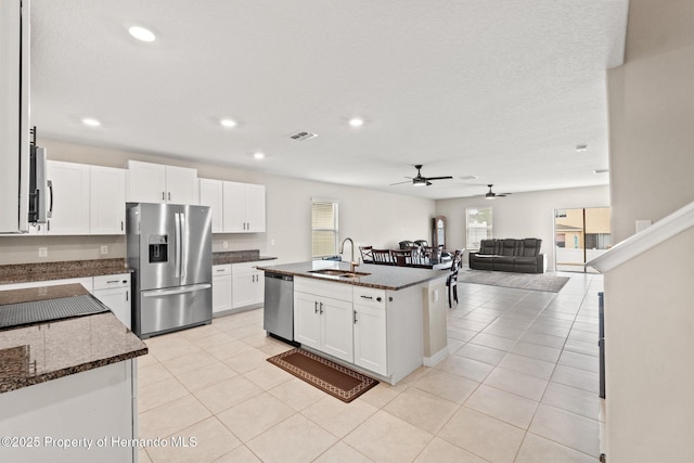 kitchen featuring sink, appliances with stainless steel finishes, white cabinetry, a center island with sink, and dark stone counters