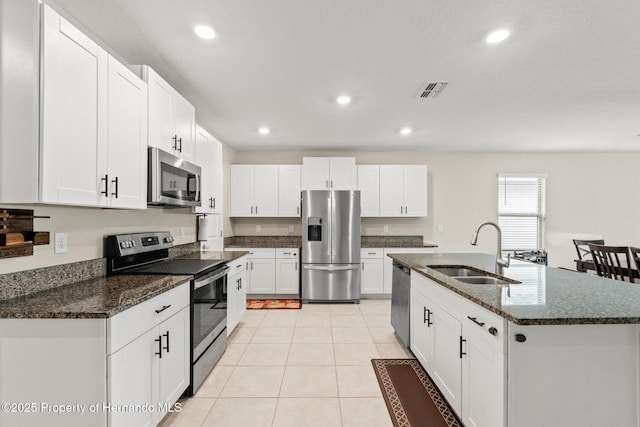 kitchen featuring sink, dark stone countertops, white cabinets, stainless steel appliances, and a center island with sink