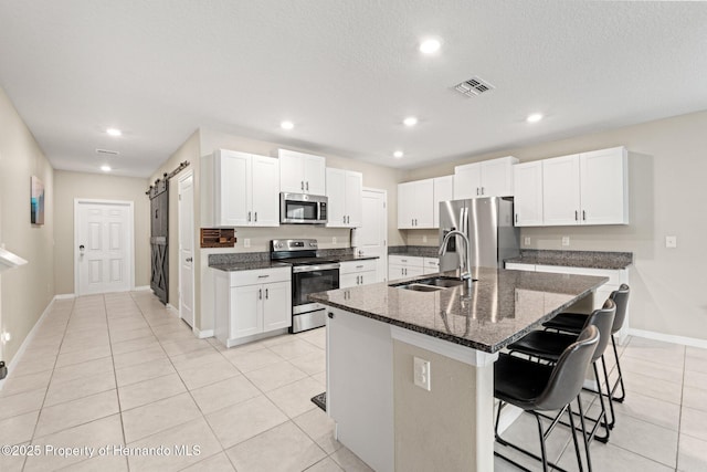 kitchen featuring sink, a kitchen island with sink, a kitchen breakfast bar, stainless steel appliances, and a barn door