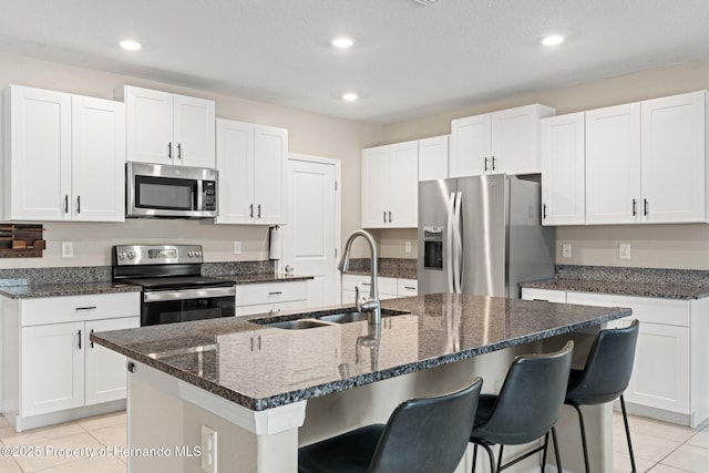 kitchen with stainless steel appliances, a kitchen island with sink, sink, and white cabinets