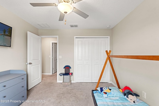 bedroom featuring ceiling fan, a closet, light carpet, and a textured ceiling