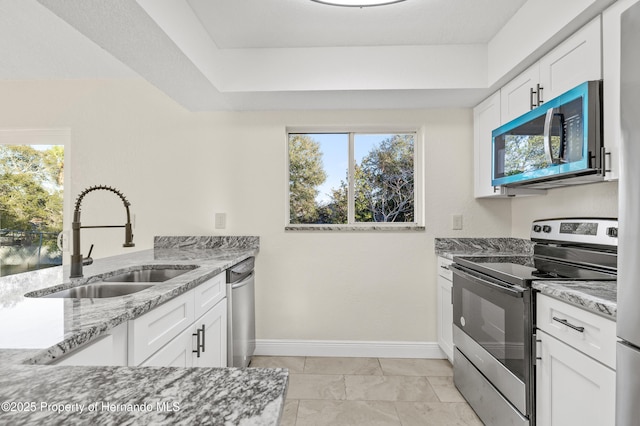 kitchen with light stone counters, stainless steel appliances, sink, and white cabinets