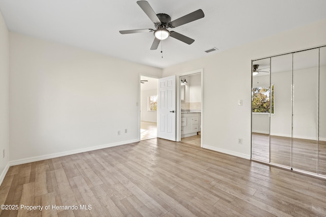 unfurnished bedroom with ceiling fan, ensuite bathroom, a closet, and light wood-type flooring