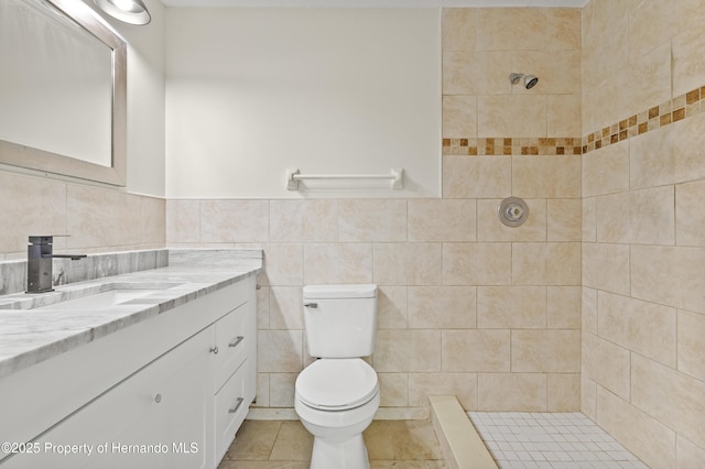 bathroom with a tile shower, tile walls, vanity, and toilet