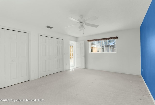 unfurnished bedroom with a ceiling fan, visible vents, multiple closets, and light colored carpet