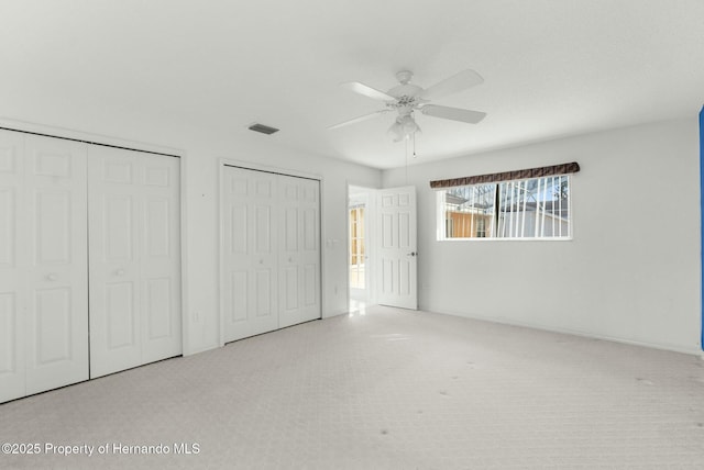 unfurnished bedroom featuring a ceiling fan, visible vents, multiple closets, and light colored carpet