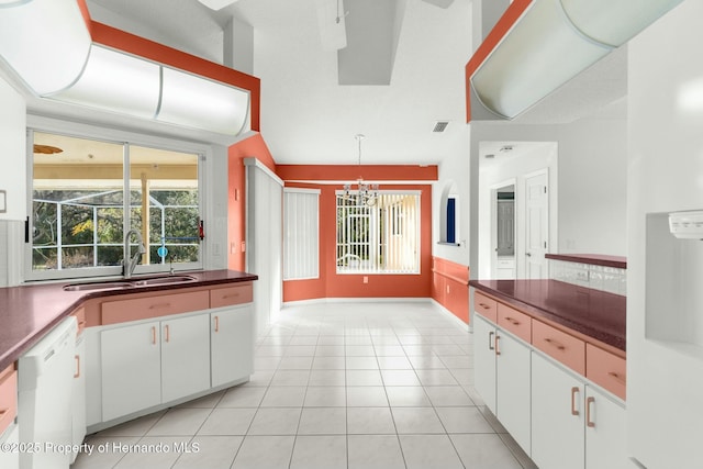 kitchen featuring dark countertops, white dishwasher, white cabinets, and a sink