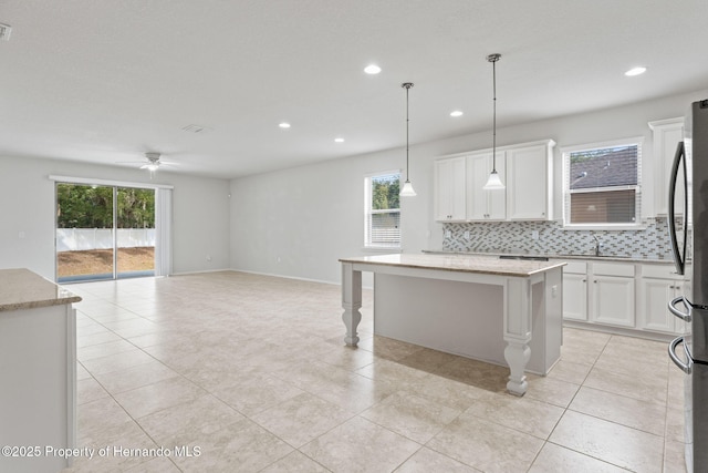 kitchen with white cabinetry, a center island, hanging light fixtures, a healthy amount of sunlight, and decorative backsplash