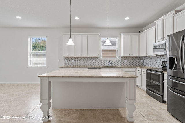 kitchen featuring stainless steel appliances, light stone countertops, white cabinets, and decorative light fixtures