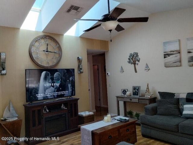 living room featuring ceiling fan, vaulted ceiling with skylight, and light wood-type flooring