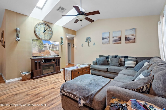 living room with ceiling fan, light hardwood / wood-style floors, and vaulted ceiling with skylight