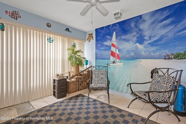 living area with ceiling fan, a water view, tile patterned floors, and a textured ceiling