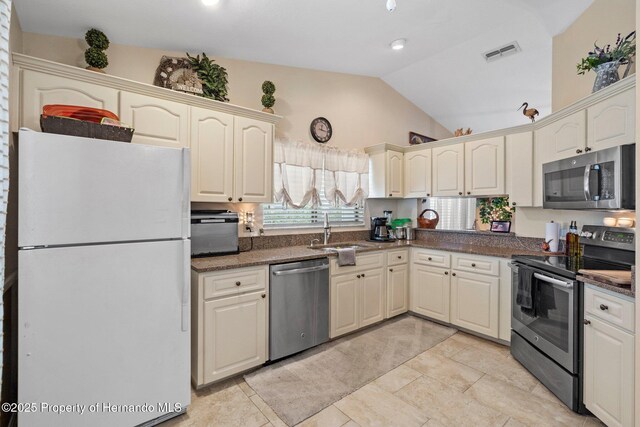 kitchen featuring lofted ceiling, sink, cream cabinets, and appliances with stainless steel finishes