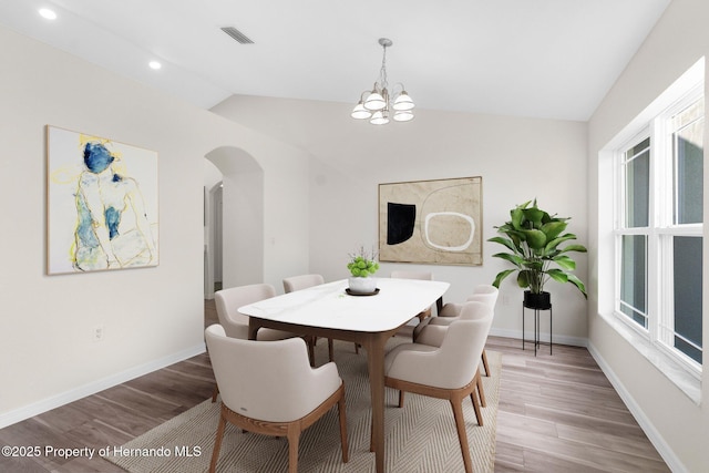 dining room featuring hardwood / wood-style flooring, vaulted ceiling, and a notable chandelier