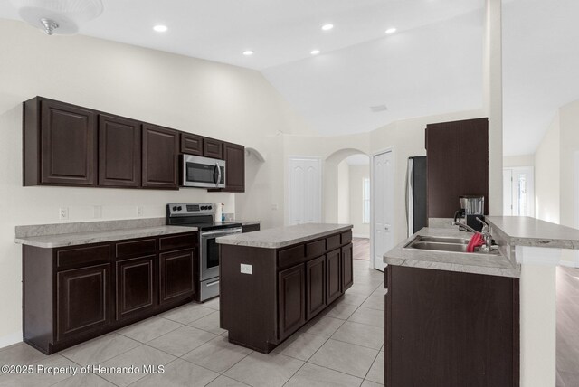 kitchen with sink, high vaulted ceiling, a center island with sink, light tile patterned floors, and appliances with stainless steel finishes