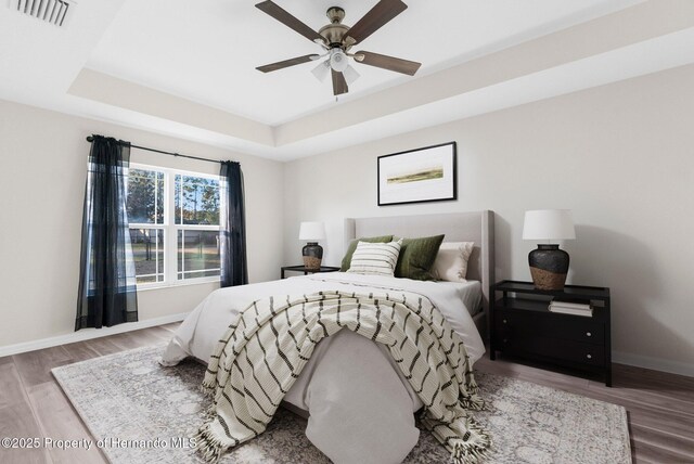 bedroom with wood-type flooring, ceiling fan, and a tray ceiling