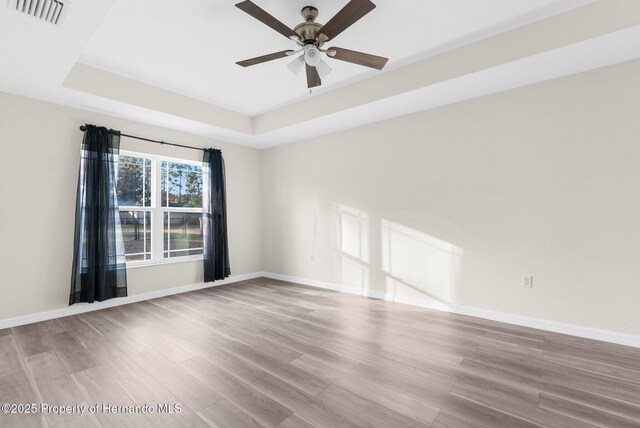 unfurnished room with a raised ceiling, hardwood / wood-style floors, and ceiling fan