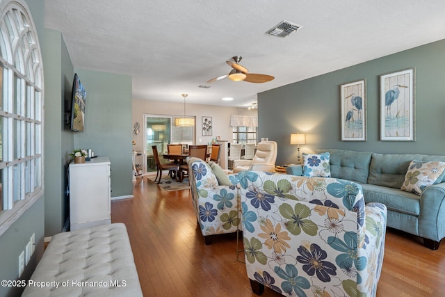 living room with hardwood / wood-style flooring, ceiling fan, and a textured ceiling