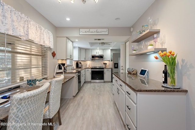 kitchen featuring sink, tasteful backsplash, light wood-type flooring, dark stone countertops, and appliances with stainless steel finishes