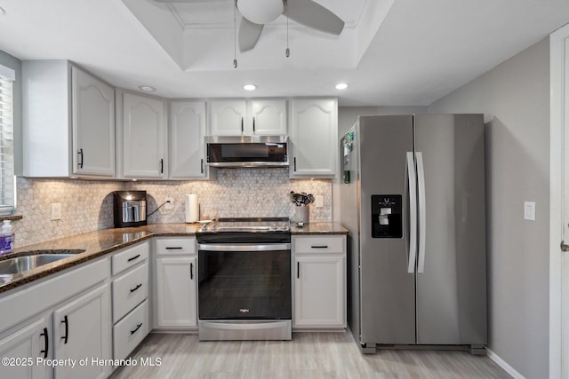 kitchen featuring white cabinetry, decorative backsplash, dark stone counters, a tray ceiling, and stainless steel appliances