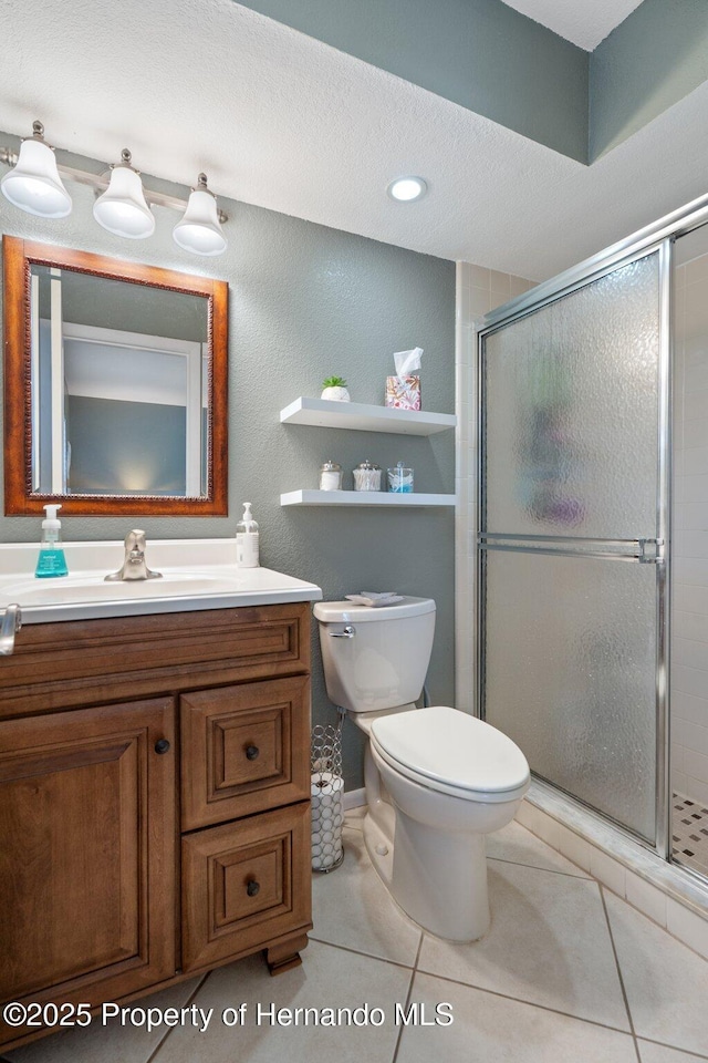 bathroom featuring tile patterned flooring, vanity, a shower with shower door, and toilet