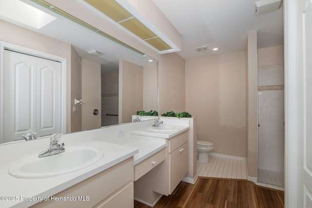 bathroom featuring a tile shower, vanity, wood-type flooring, and toilet