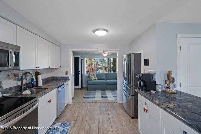 kitchen featuring sink, appliances with stainless steel finishes, dark stone countertops, backsplash, and white cabinets