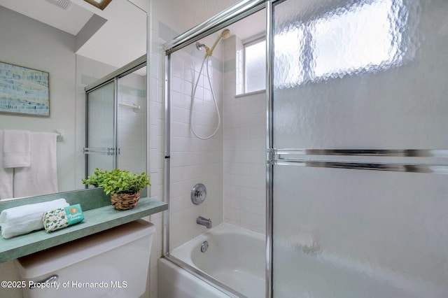 bathroom featuring toilet and combined bath / shower with glass door