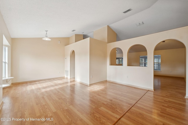 spare room featuring vaulted ceiling, a textured ceiling, and light hardwood / wood-style floors