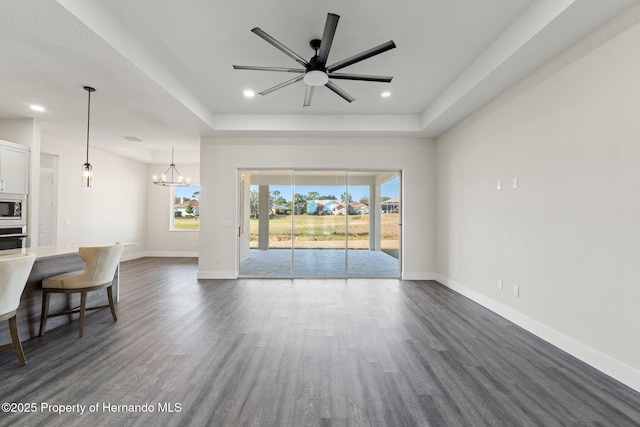 unfurnished living room with dark wood-type flooring, a raised ceiling, and ceiling fan with notable chandelier