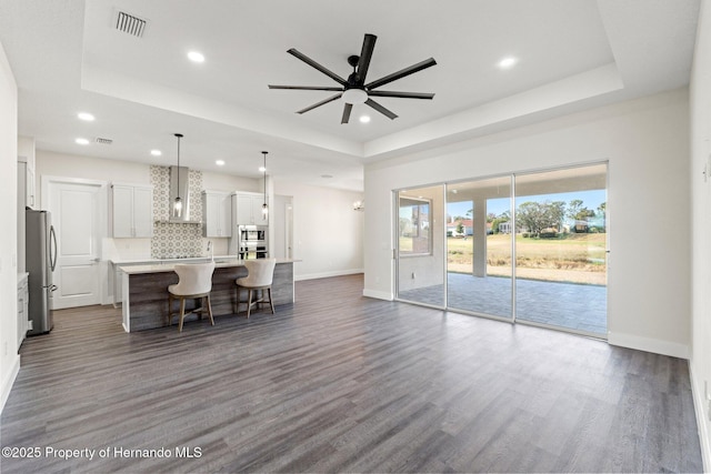 kitchen with decorative light fixtures, a tray ceiling, stainless steel appliances, and a center island with sink