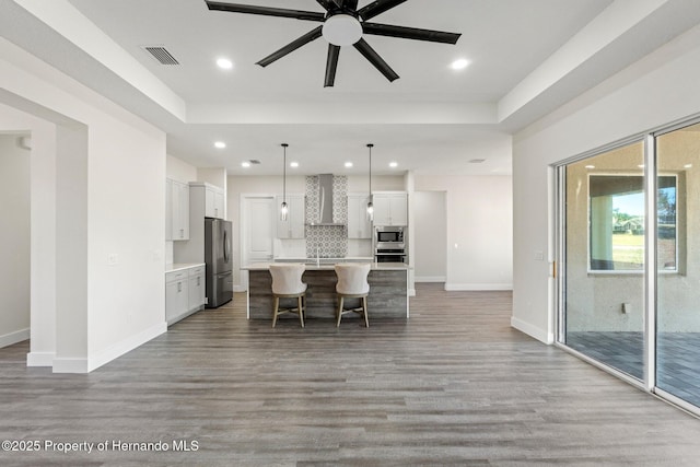 kitchen featuring appliances with stainless steel finishes, pendant lighting, white cabinetry, a center island with sink, and wall chimney exhaust hood