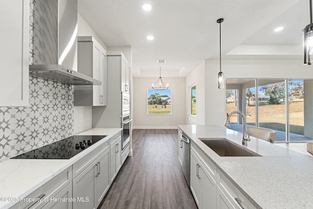 kitchen with pendant lighting, sink, stainless steel appliances, light stone countertops, and wall chimney exhaust hood