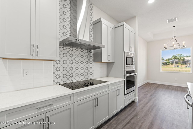 kitchen with light stone counters, decorative light fixtures, appliances with stainless steel finishes, dark hardwood / wood-style floors, and wall chimney range hood