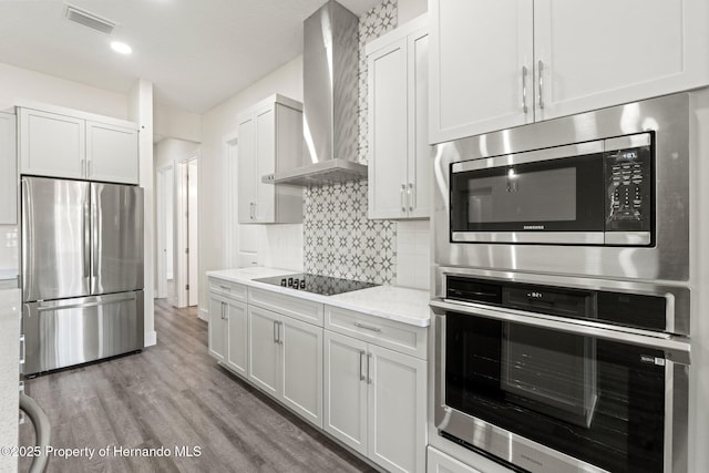 kitchen featuring light stone counters, wall chimney range hood, stainless steel appliances, and white cabinets